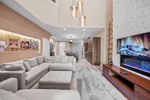 A modern living room with a sectional sofa, a flat-screen TV, and a decorative wall. - 4BR house sleeps 10 in Magic Village Views (Kissimmee)