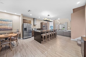 A modern kitchen with a central island, stainless steel appliances, and a dining area with wooden chairs. - 4BR house sleeps 10 in Magic Village Views (Kissimmee)