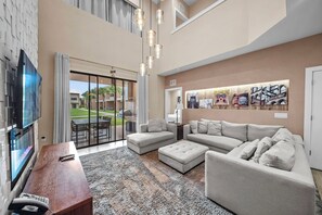 A spacious living room with a large sectional sofa, a flat-screen TV mounted on the wall, and a dining area with a table and chairs. - 4BR house with private hot tub in kissimmee (Kissimmee)