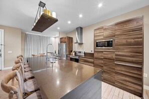 A modern kitchen with a large island, stainless steel appliances, and a wood-patterned cabinet. - 4BR house sleeps 10 in Magic Village Views (Kissimmee)