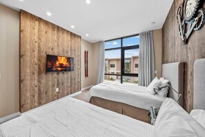 Une chambre d’hôtel avec deux lits, une cheminée, une grande fenêtre et une horloge au mur.