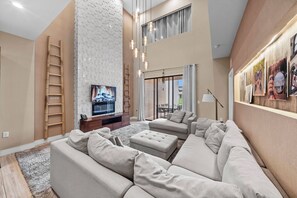 A spacious living room with a sectional sofa, a flat-screen TV, and a fireplace. - 4BR house sleeps 10 in Magic Village Views (Kissimmee)