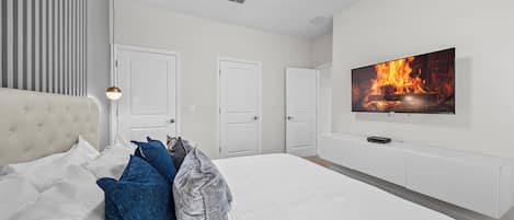 A bedroom with a large bed, a TV mounted on the wall, and three doors.