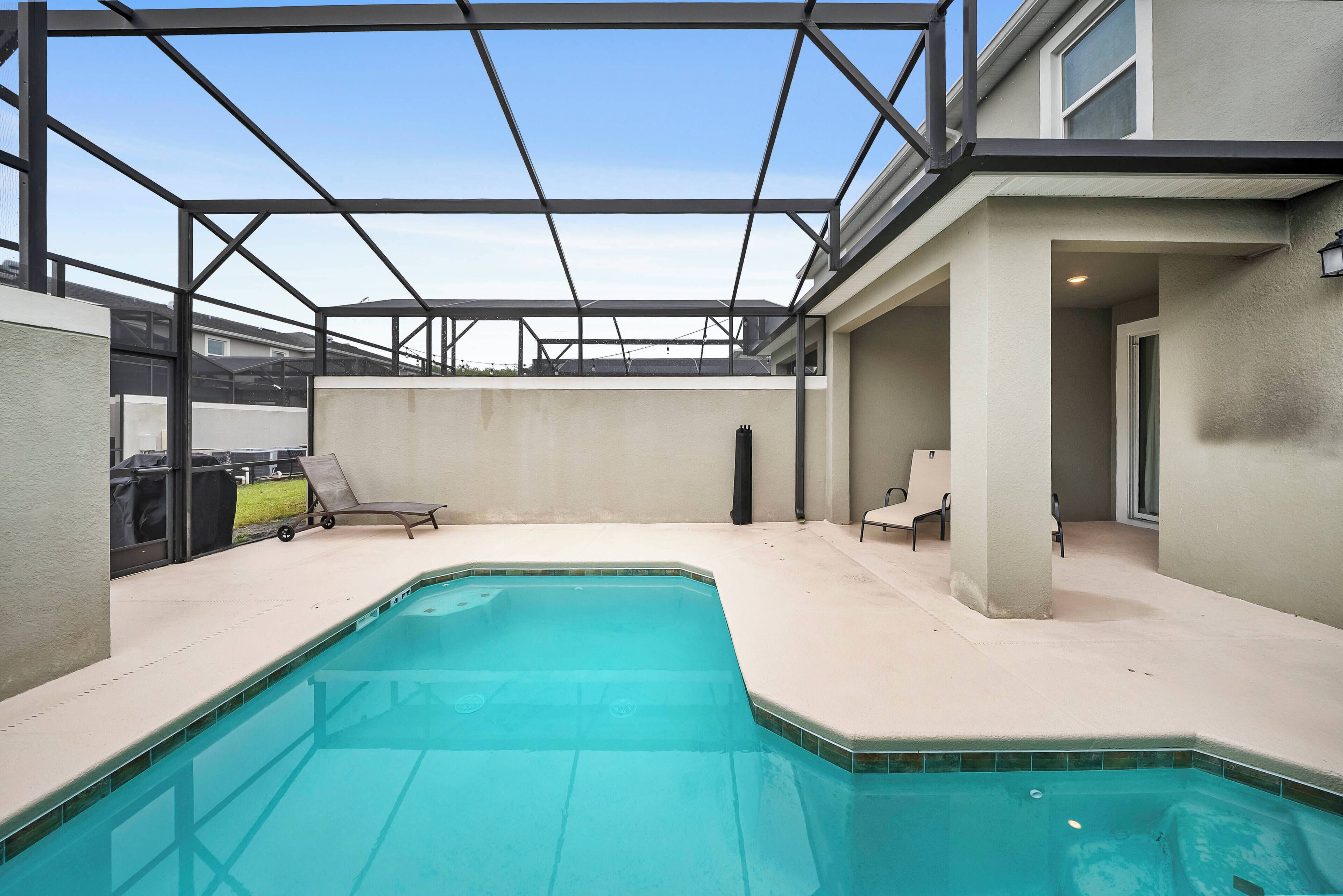 A swimming pool with a covered patio area, lounge chairs, and a view of the surrounding neighborhood.