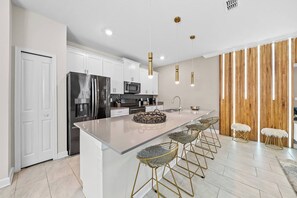 A modern kitchen with a central island, stainless steel appliances, and bar stools. - 4BR house sleeps 8 with private pool (Kissimmee)