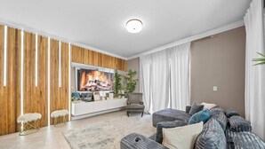 A modern living room with a flat-screen TV, wooden panel wall, grey sofa, and a white rug. - 4BR house sleeps 8 with private pool (Kissimmee)