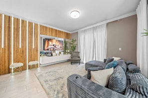 A modern living room with a flat-screen TV, wooden panel wall, grey sofa, and a white rug. - 4BR house sleeps 8 with private pool (Kissimmee)