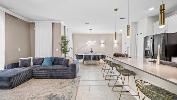 A modern living room with a sectional sofa, a dining area with a table and chairs, and a kitchen with a refrigerator and bar stools. - 4BR house sleeps 8 with private pool (Kissimmee)