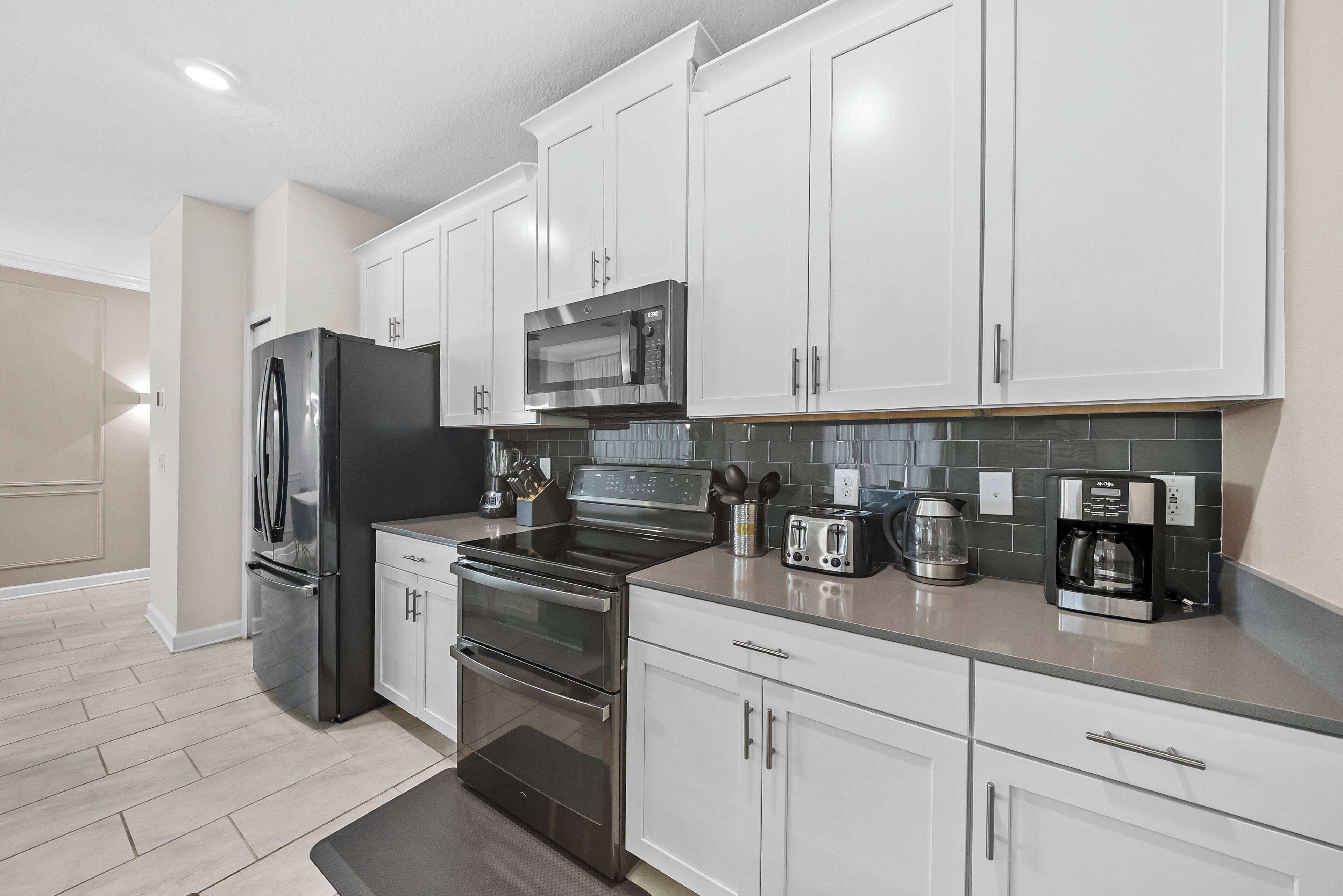 A modern kitchen with stainless steel appliances, white cabinetry, and a tiled backsplash.