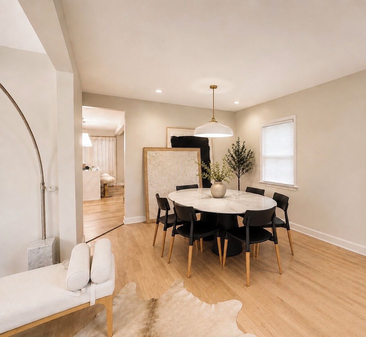 A modern dining area with a round table, black chairs, a pendant light, and a wooden floor.