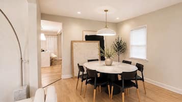 A modern dining area with a round table, black chairs, a pendant light, and a wooden floor.