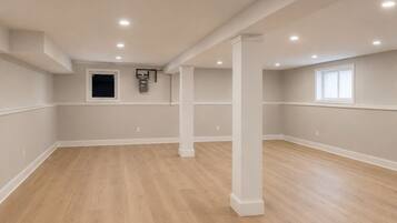 A spacious room with wooden flooring, white walls, and a window.