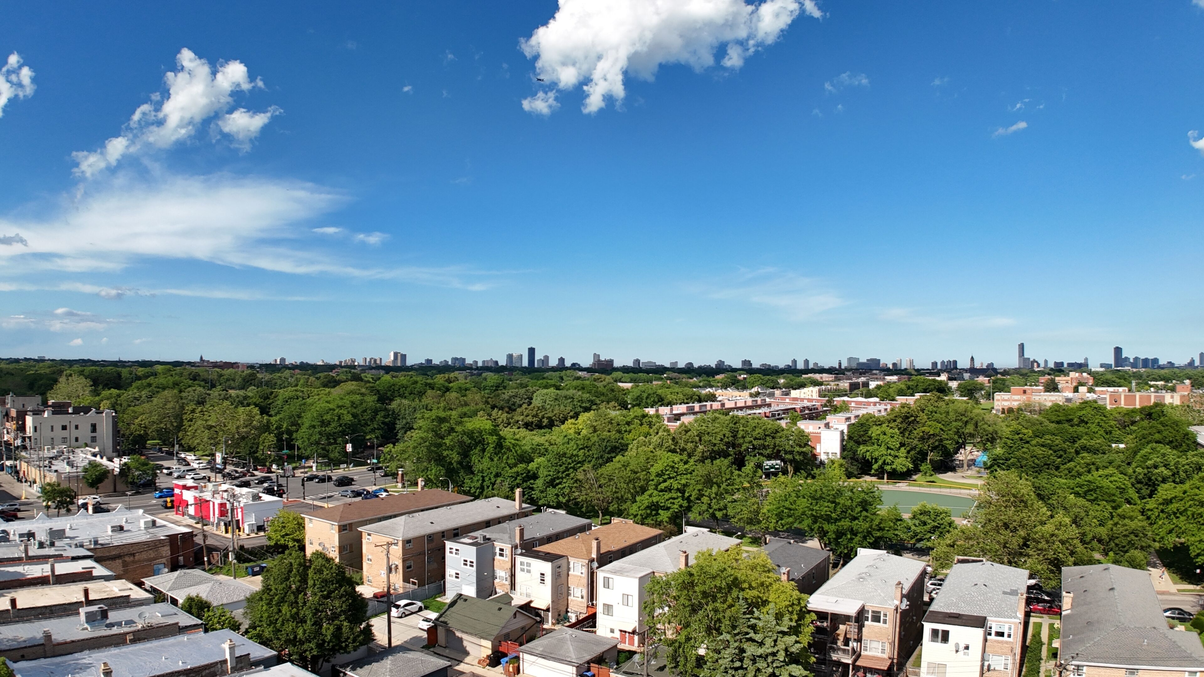 A residential area with multiple-story buildings, a clear sky, and a distant city skyline.