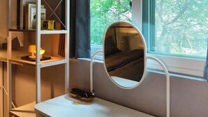 Ein Zimmer mit weißem Schreibtisch, einem Spiegel und einem Fenster mit Blick auf Bäume.