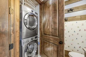 A laundry room with stacked washers and dryers, wooden doors, and a wall with a ski-themed decal. - Dogwood and Stone Luxury 2BR Mountain Escape 3K (Park City)
