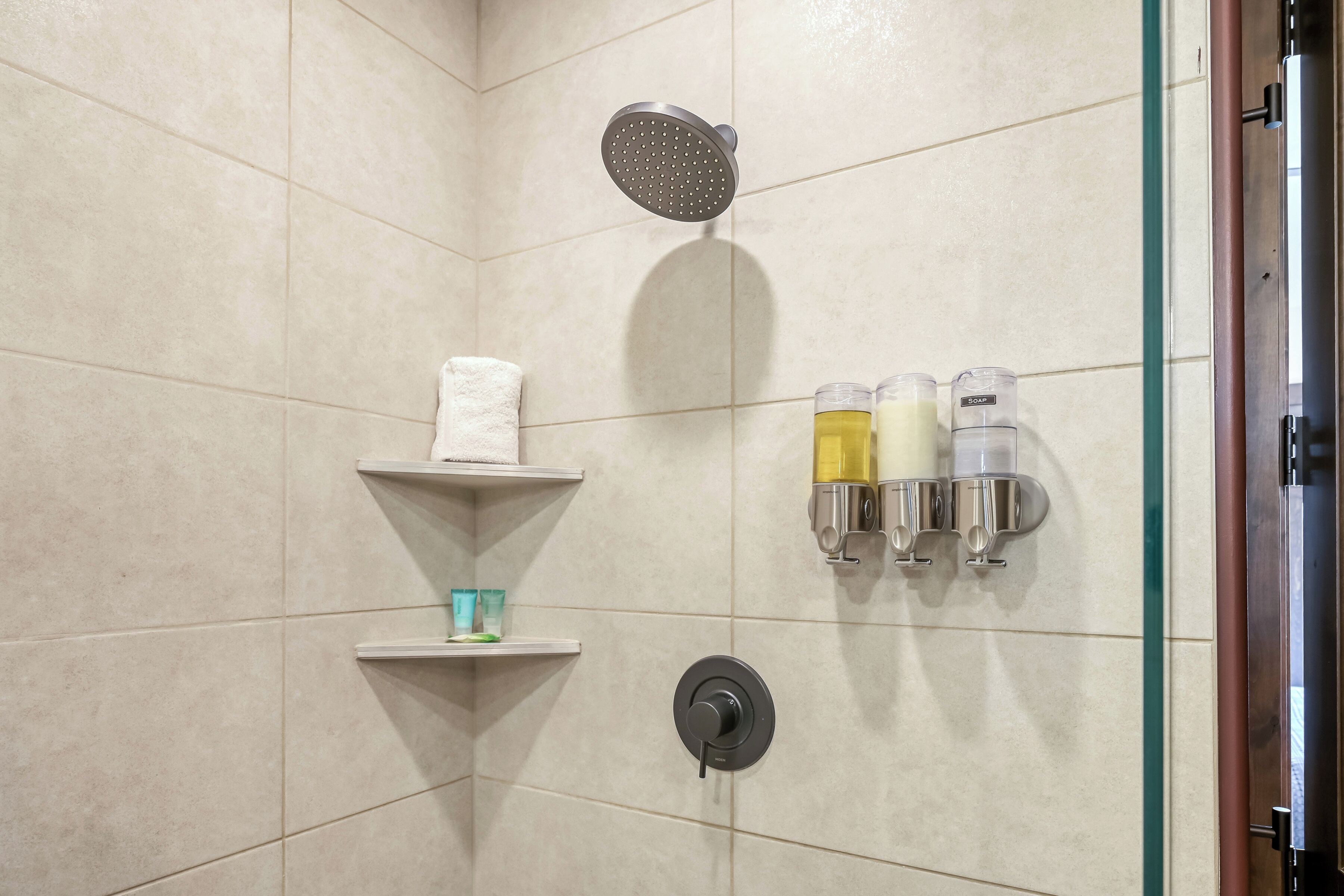 A shower area with a handheld showerhead, a towel rack with a towel, and soap dispensers.