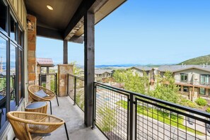 A balcony with wicker chairs, a stone wall, and a view of a residential area with houses and hills. - Dogwood and Stone Luxury 2BR Mountain Escape 3K (Park City)