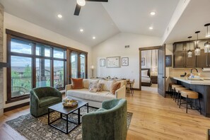 A spacious living area with a sofa, chairs, a dining table, and a kitchen area with bar stools. - Dogwood and Stone Luxury 2BR Mountain Escape 3K (Park City)