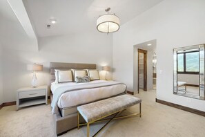 A bedroom with a bed, bedside tables, a bench, a large mirror, and a view of a balcony. - 1491 April Mountain Drive (Park City)
