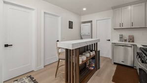 A compact kitchen with white cabinets, a built-in oven, and a small dining area with a white table and chairs. - Walk to Beach (3 Blks)! 2BR/2-Beds PB Gem + AC - Holiday Home (San Diego)