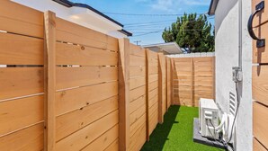A narrow outdoor space with wooden fences, a small artificial turf area, and a white wall with a metal gate. - Walk to Beach (3 Blks)! 2BR/2-Beds PB Gem + AC - Holiday Home (San Diego)