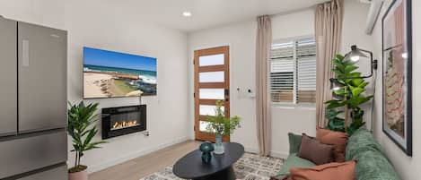A modern living room with a flat-screen TV, a fireplace, a sofa, and a dining table.