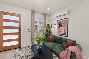 A modern living room with a green sofa, a coffee table, a potted plant, and a framed artwork on the wall. - Walk to Beach (3 Blks)! 2BR/2-Beds PB Gem + AC - Holiday Home (San Diego)