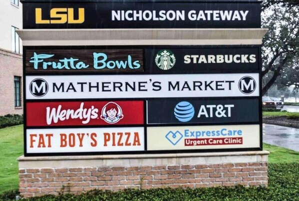 Ein Schild mit verschiedenen Firmenlogos, darunter LSU, Frutta Bowls, Starbucks, Matherne's Market, Wendy's, AT&T, Fat Boy's Pizza und ExpressCare Ambulanz.