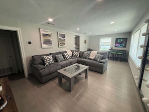Ein Wohnzimmer mit Ecksofa, einem Glastisch und einem Essbereich mit kleinem Tisch und Stühlen.