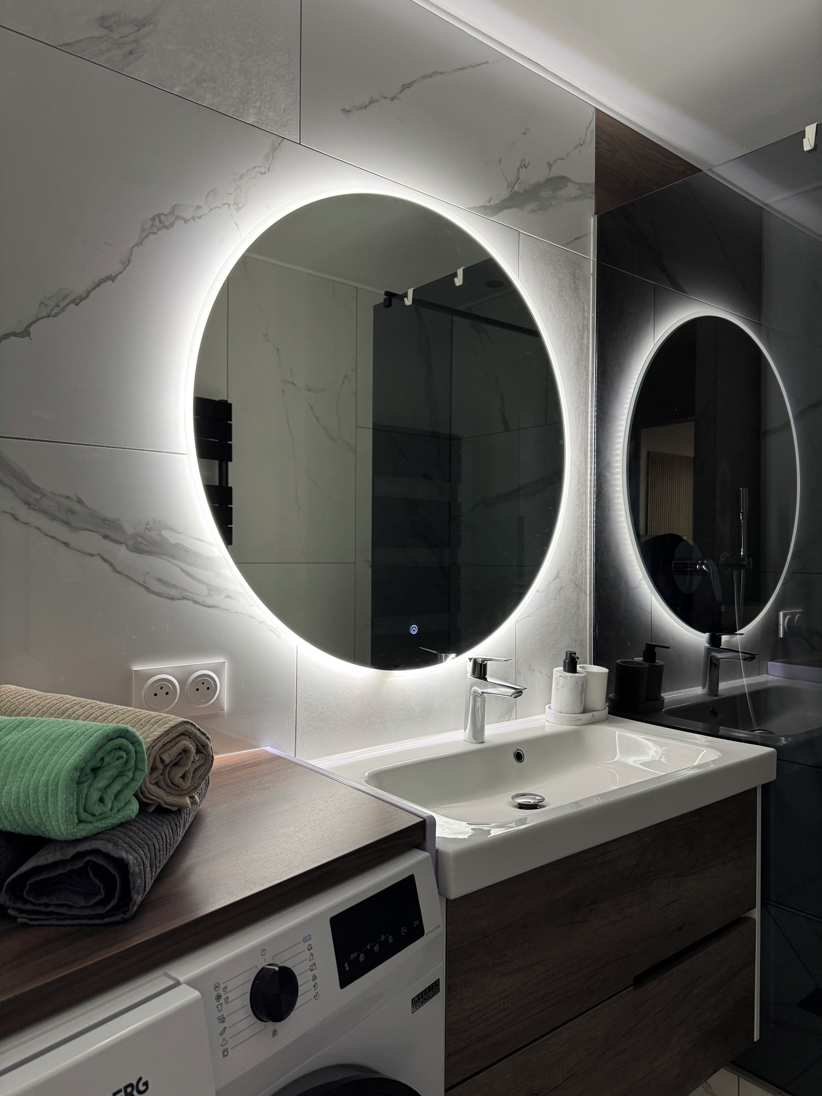 Une salle de bain moderne avec un grand miroir, un lavabo et un lave-linge.