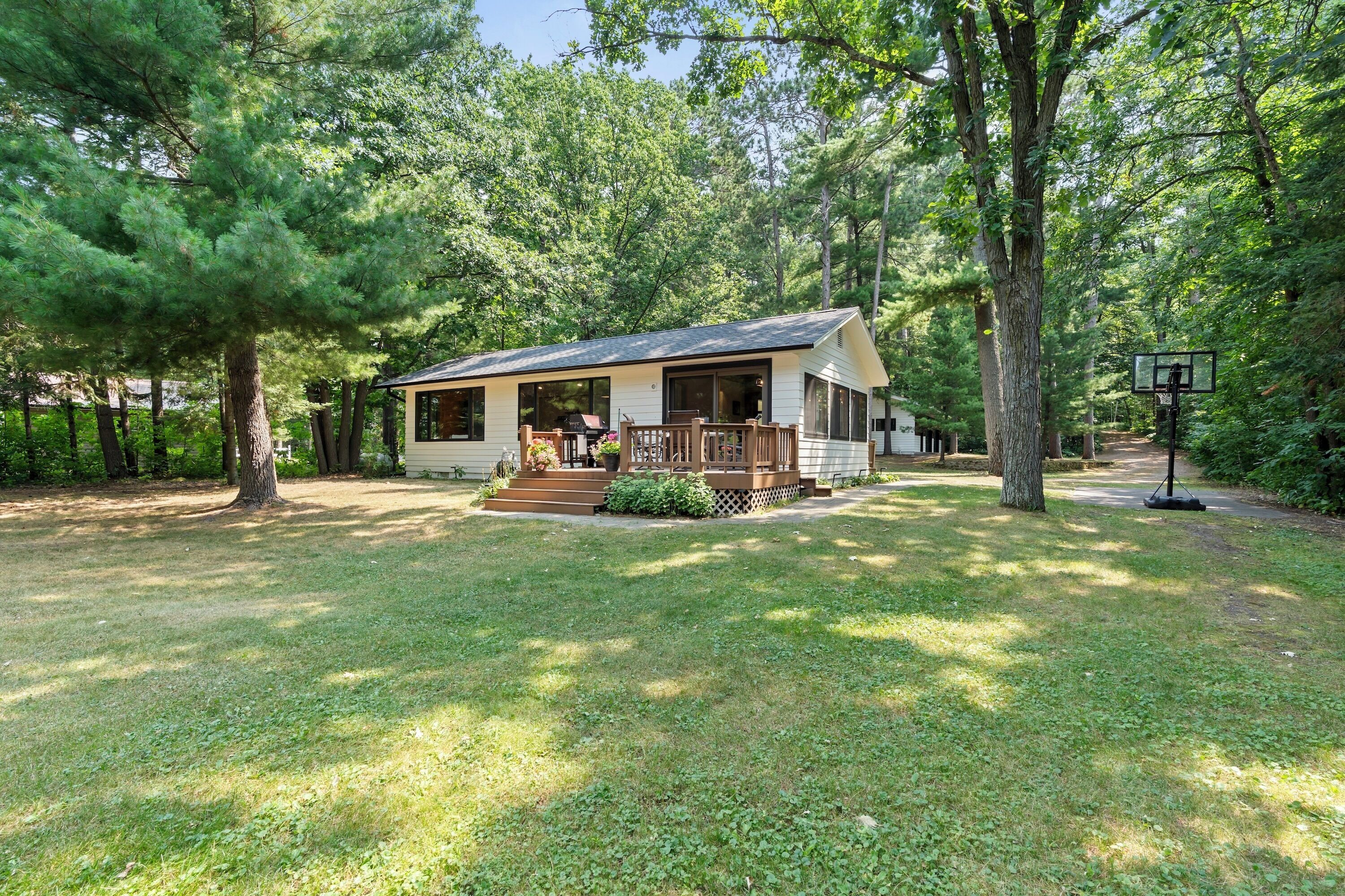 A small cabin with a porch, surrounded by trees and a grassy yard.