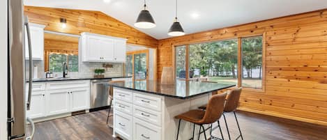 A modern kitchen with wooden walls, white cabinets, a large island with bar stools, and a view of the outdoors.