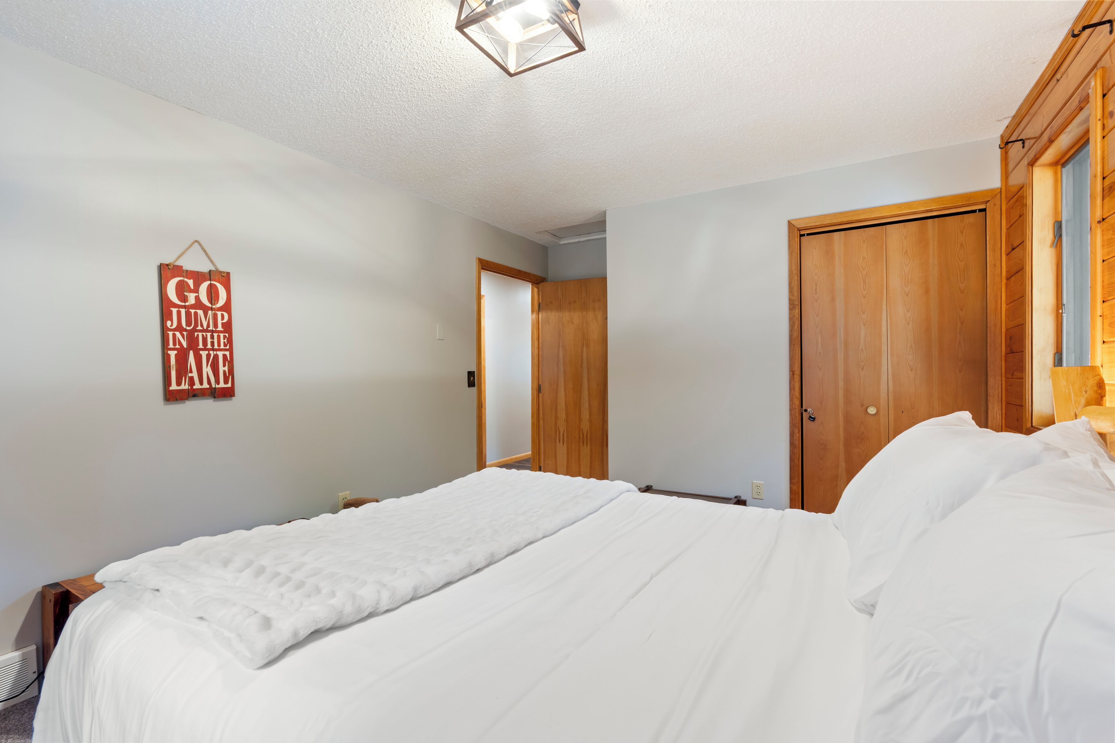 A bedroom with a bed, a wooden wardrobe, a door, and a wall-mounted sign.