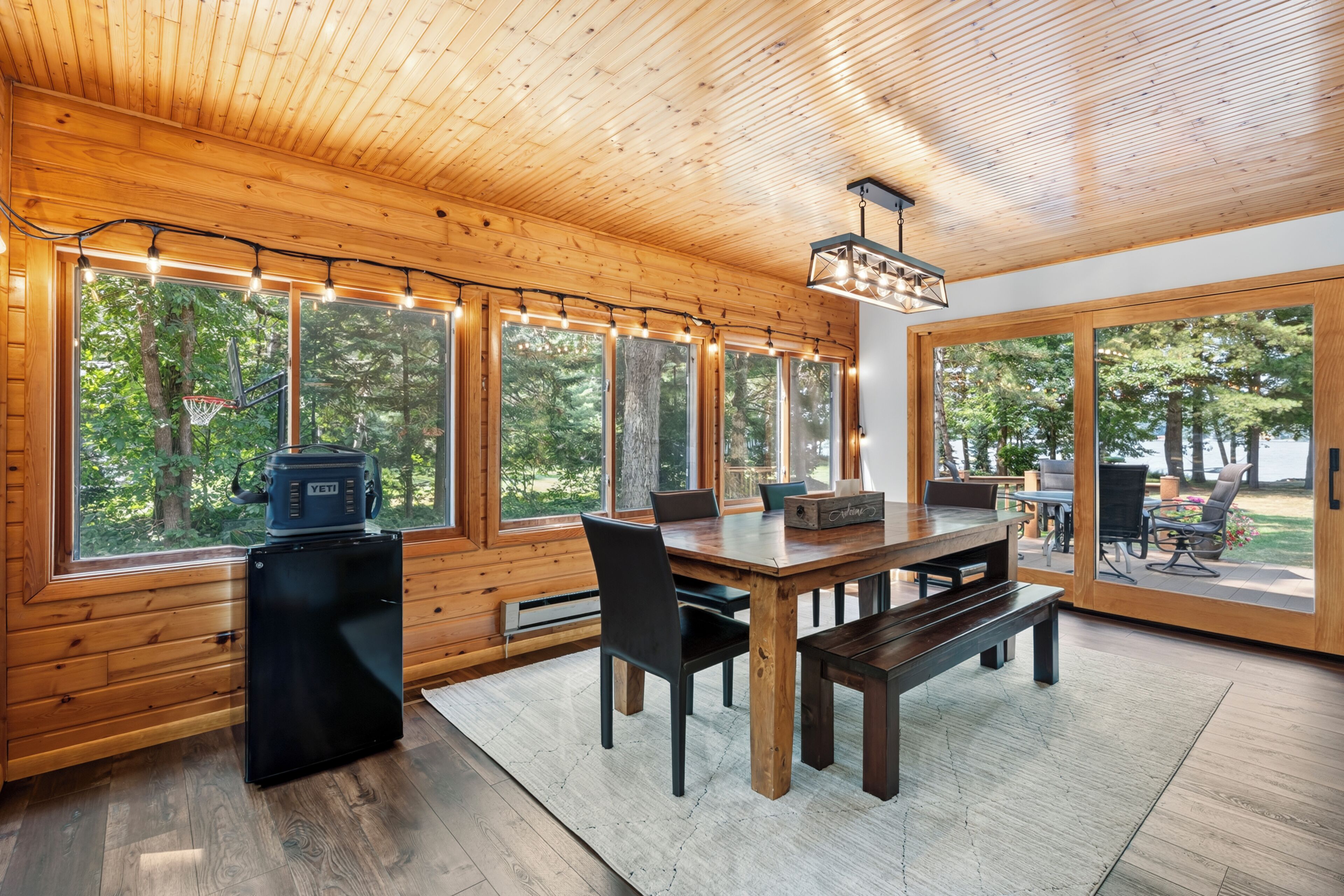 Un interior de madera con zona de comedor, ventanas grandes y vistas al exterior.