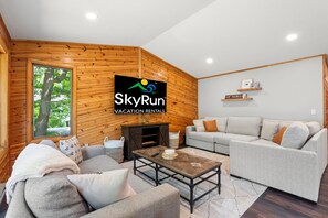 Ein gemütliches Wohnzimmer mit einer Holzwand, einem Sofa, einem Couchtisch und einem Fernseher, der das SkyRun Logo zeigt.