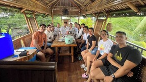 A group of people seated around a table in a bamboo hut with a thatched roof, surrounded by lush greenery. - Room-luxurious Villa Rental in Umingan w (Umingan)