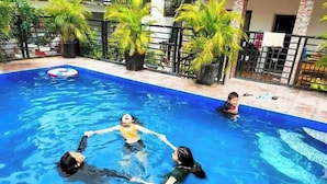 A swimming pool with three people in the water, surrounded by potted plants and a fence. - Room-luxurious Villa Rental in Umingan w (Umingan)