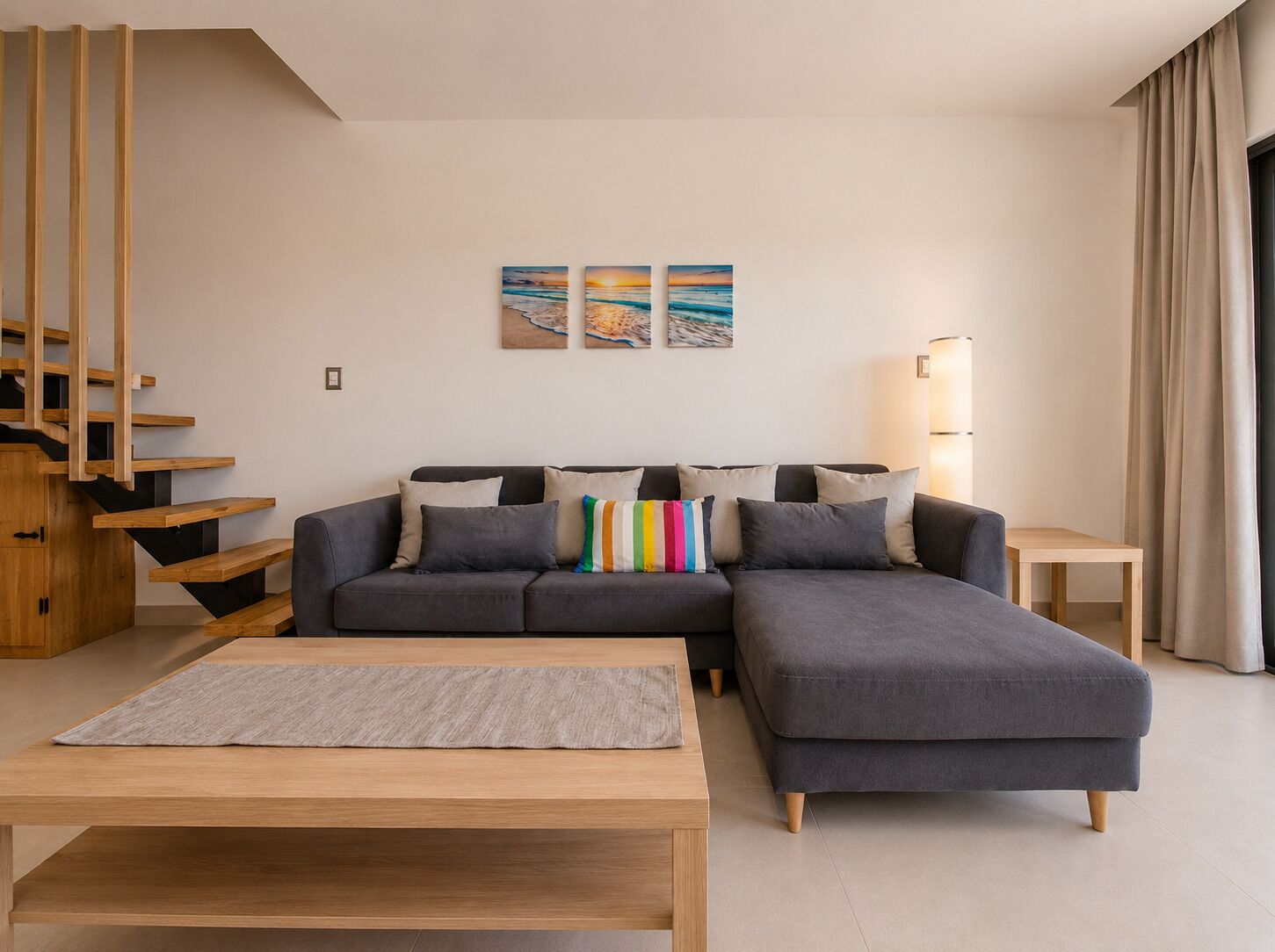 A modern living room with a grey sectional sofa, a wooden coffee table, and a staircase with wooden railings.