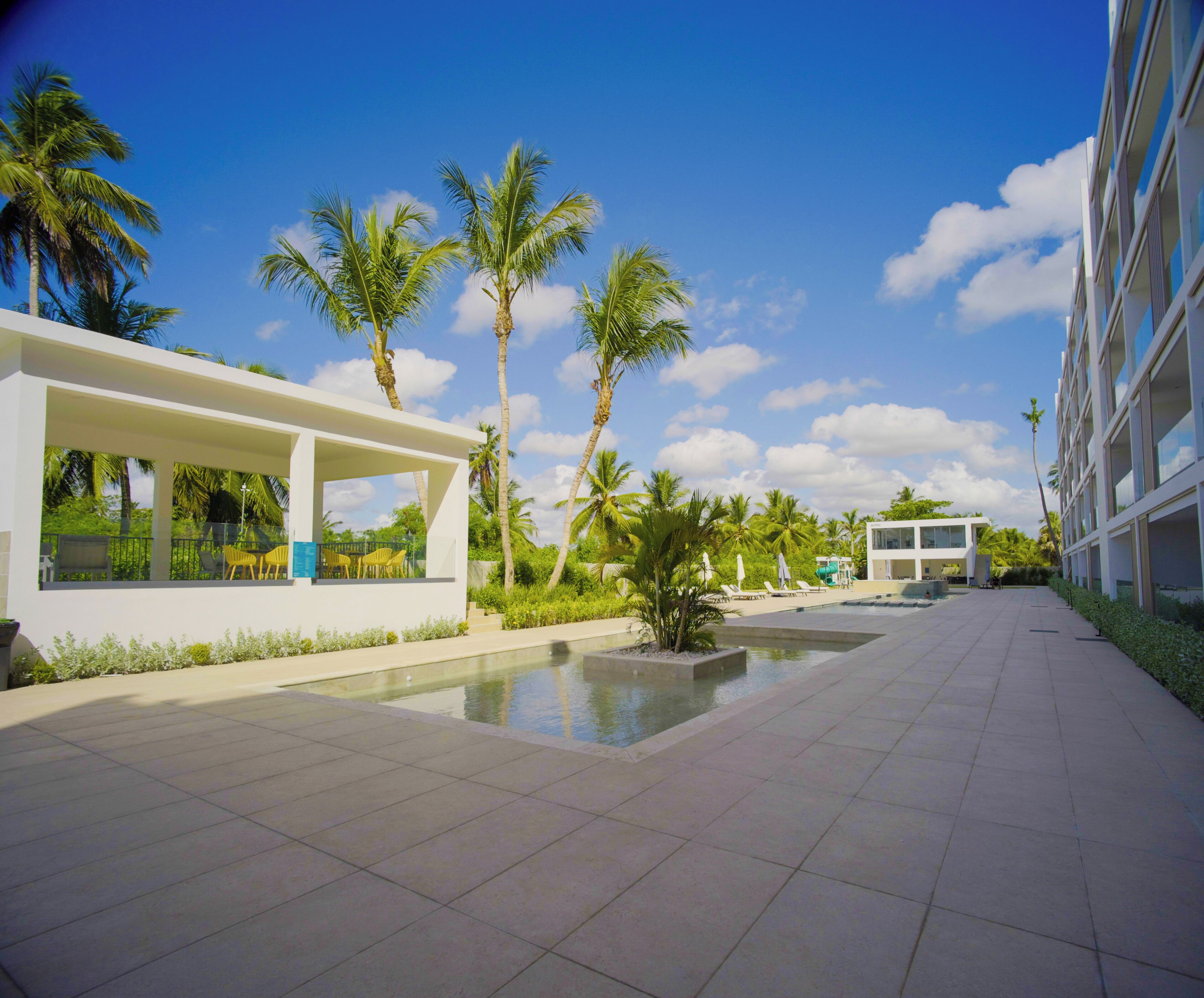 A modern hotel with a pool, palm trees, and a clear blue sky.