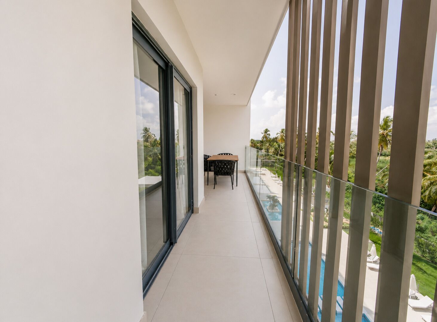 Ein Balkon mit Glasgeländer, der einen Blick auf ein Schwimmbecken und üppiges Grün bietet.