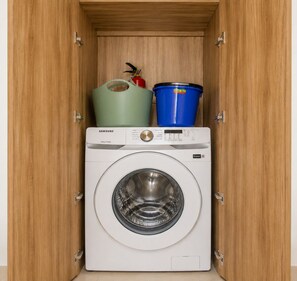 A Samsung washing machine in a wooden cabinet with a green and blue bucket on top. - BORN Villa Laguna Vista Is Your Home Away From Home in Paradise! (Punta Cana)