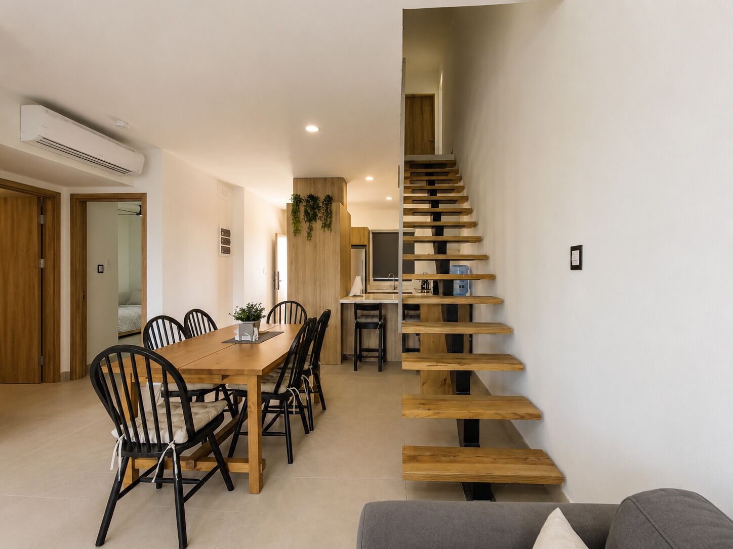 A modern interior with a dining area, staircase, and a kitchenette.