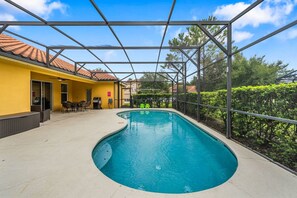 Une piscine dotée d’un espace couvert, un bâtiment jaune et un jardin clôturé.