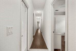Ein schmaler, gut beleuchteter Flur mit Holzboden, weißen Wänden und einer Tür am Ende, die zu einem Badezimmer führt.