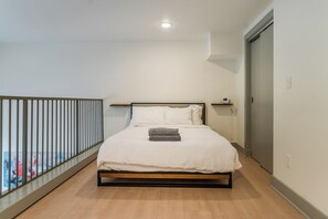 A bedroom with a bed, a bedside table, a wall-mounted shelf, and a balcony railing. - Downtown Loft Retreat - Nearby Parking - 2F (Louisville)