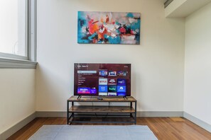Ein Zimmer mit Flachbildfernseher auf einem Holzständer, einem Bild an der Wand und einem Fenster.