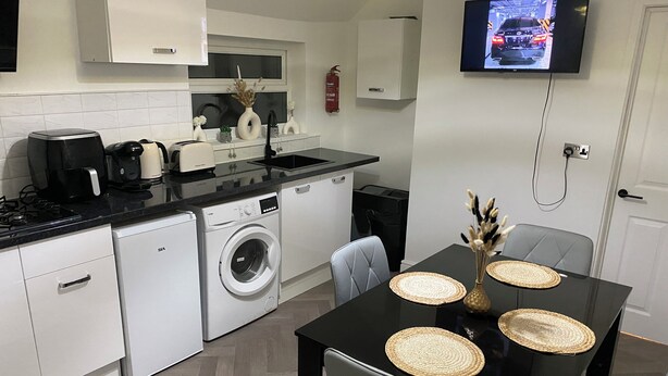 A compact kitchen with a washing machine, a coffee maker, and a TV mounted on the wall. - Prestige 3 bedroom flat in Cardiff (Cardiff)