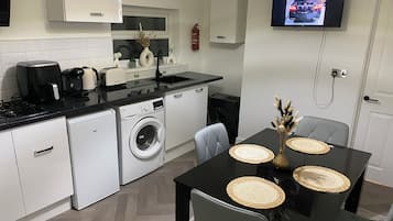 A compact kitchen with a washing machine, a coffee maker, and a TV mounted on the wall.