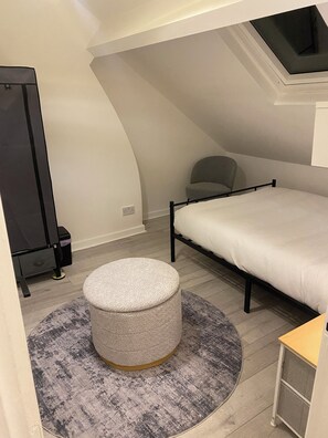Ein Schlafzimmer mit einem Bett, einem runden Hocker, einem Sessel und einem Kleiderschrank.