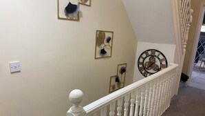 A staircase with a white balustrade, a wall-mounted clock, and decorative wall art. - Prestige 3 bedroom flat in Cardiff (Cardiff)